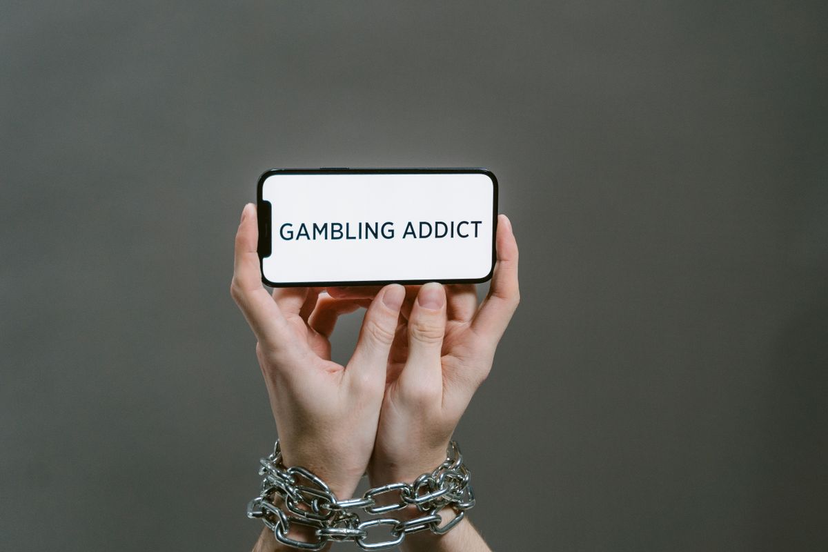 Chained hands holding a phone displaying Gambling Addict