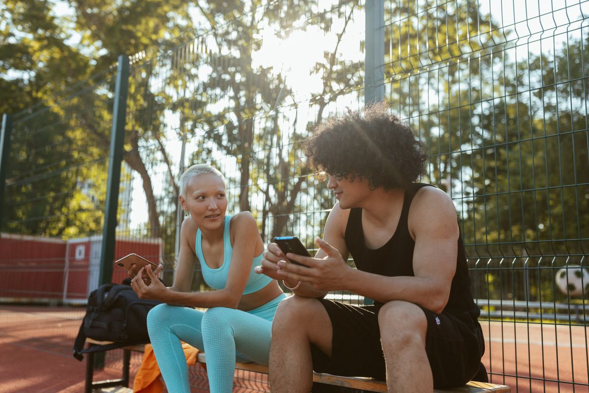 Young friends relaxing on a basketball court with smartphones